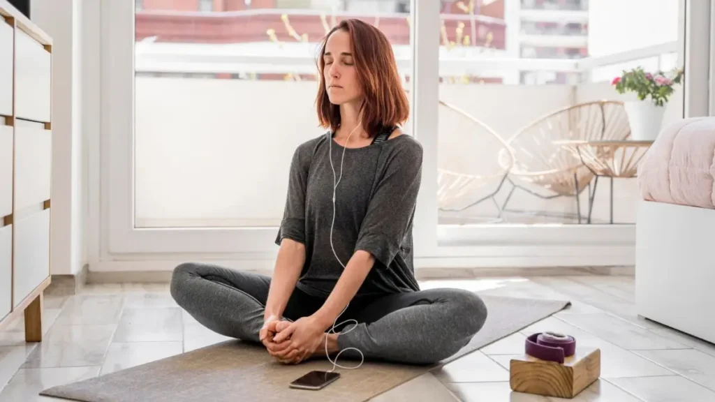 mulher sentada confortavelmente durante uma prática curta de meditação, olhos fechados, postura natural, celular colocado de lado sem estar sendo usado, luz suave