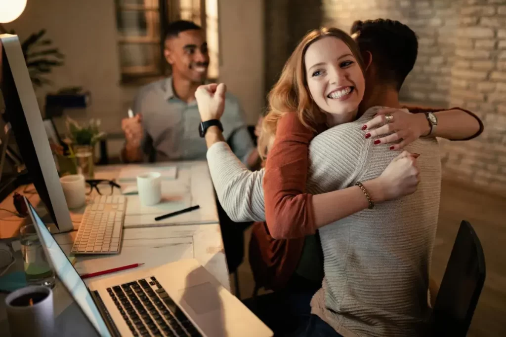 Feliz empresária abraçando seu colega de trabalho enquanto comemora o sucesso no escritório Imagem de Drazen Zigic no Freepik.