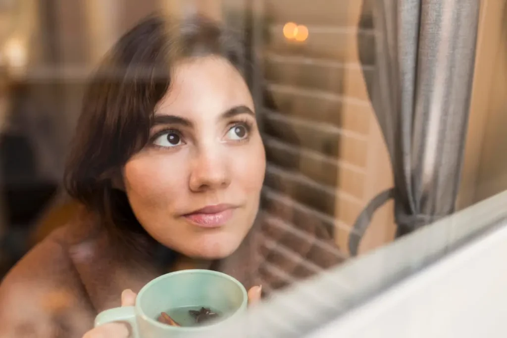 _Mulher jovem acolhida por um cobertor, segurando uma xícara de café (Fonte Freepik)