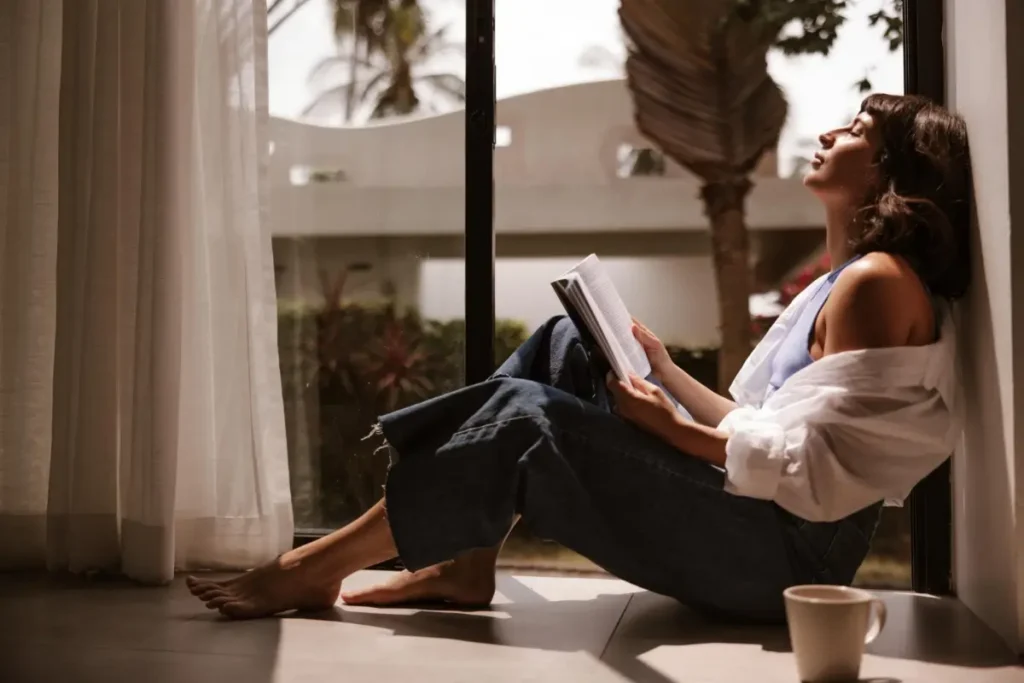 Mulher relaxando, lendo um livro, sob a luz do sol, em paz. Freepik.
