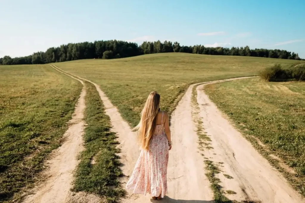 Mulher diante de dois caminhos refletindo sobre qual direção seguir. Imagem gerada por IA.